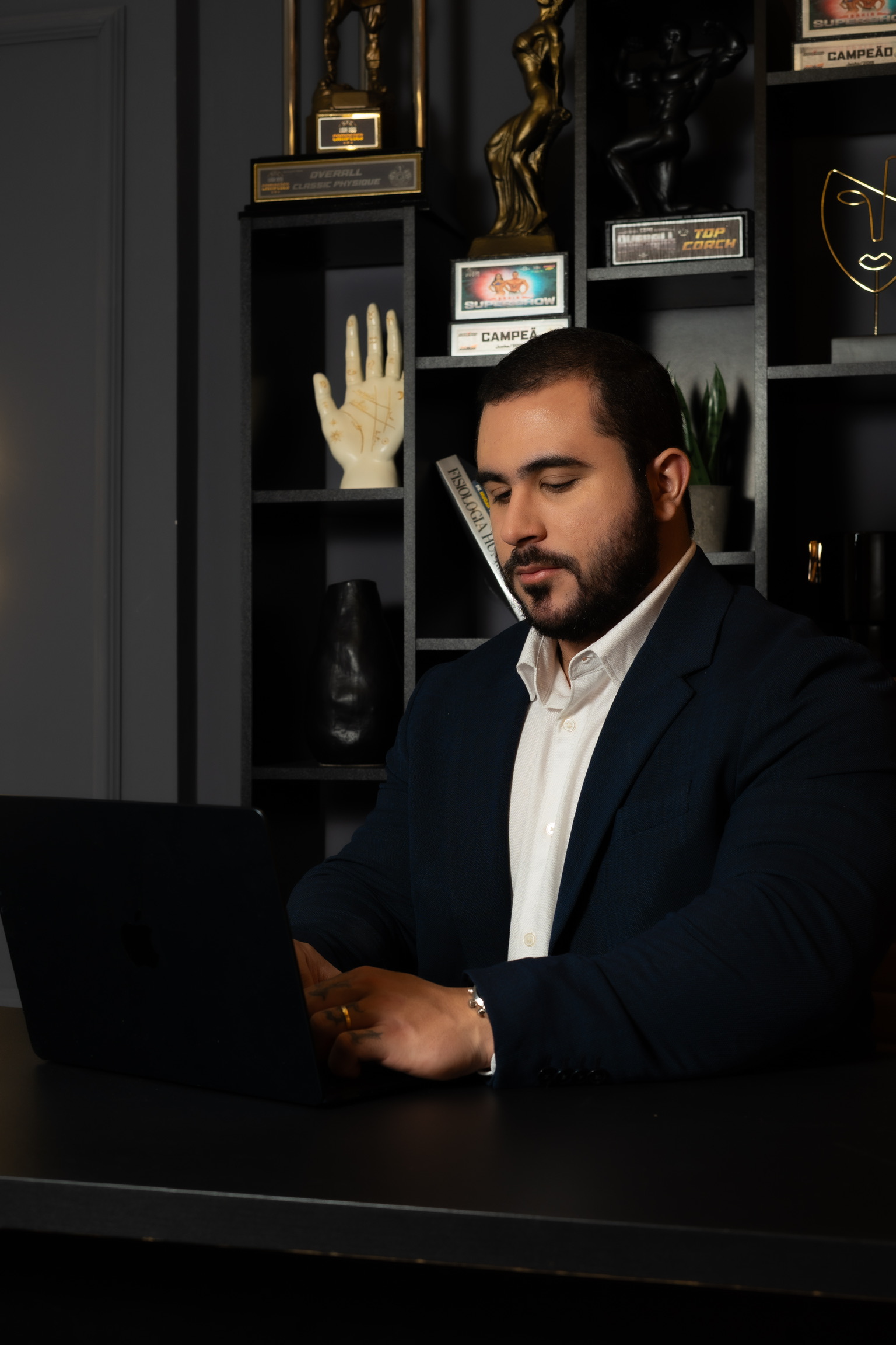 Gabriel Miranda trabalhando em plano alimentar com troféus de fisiculturismo ao fundo